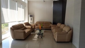 A modern living room with a sectional sofa, a coffee table, and a large window providing natural light. - Bangka City Hotel (Pangkalpinang)