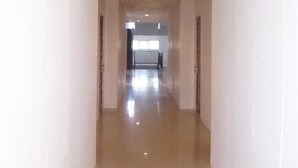 A long, narrow hallway with white walls and a shiny floor, leading to a room with a window and a railing. - Bangka City Hotel (Pangkalpinang)