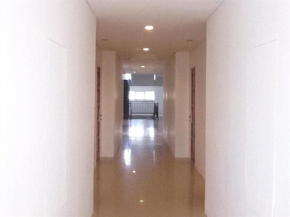 A long, narrow hallway with white walls and a shiny floor, leading to a room with a window and a railing. - Bangka City Hotel (Pangkalpinang)