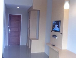 A hallway with a wooden door, a recessed shelf, and a mounted television. - Bangka City Hotel (Pangkalpinang)