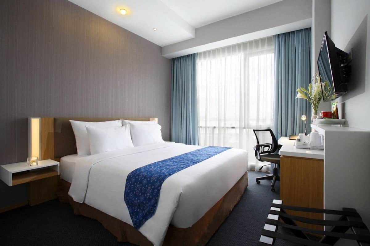 A hotel room with a bed, desk, chair, TV, and a window with curtains.
