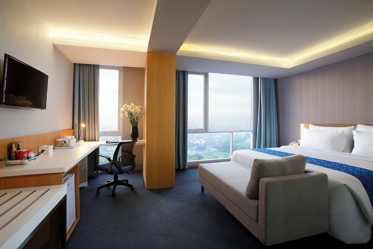 A hotel room with a bed, a desk, a chair, a television, and a large window.