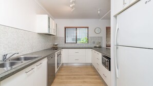 Et moderne køkken med hvide skabe, granitbordplader, rustfrie stålapparater, et vindue med persienner og et ur på væggen.