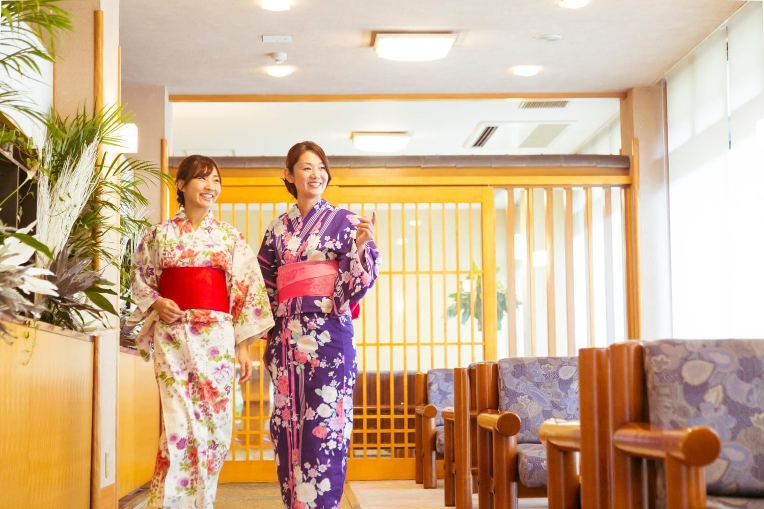 Duas pessoas vestidas com quimonos tradicionais japoneses em uma sala com móveis de madeira e uma porta deslizante.
