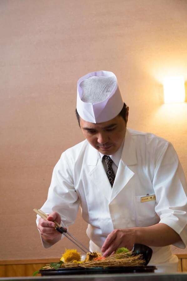 A person in a white uniform and hat preparing food on a tray.