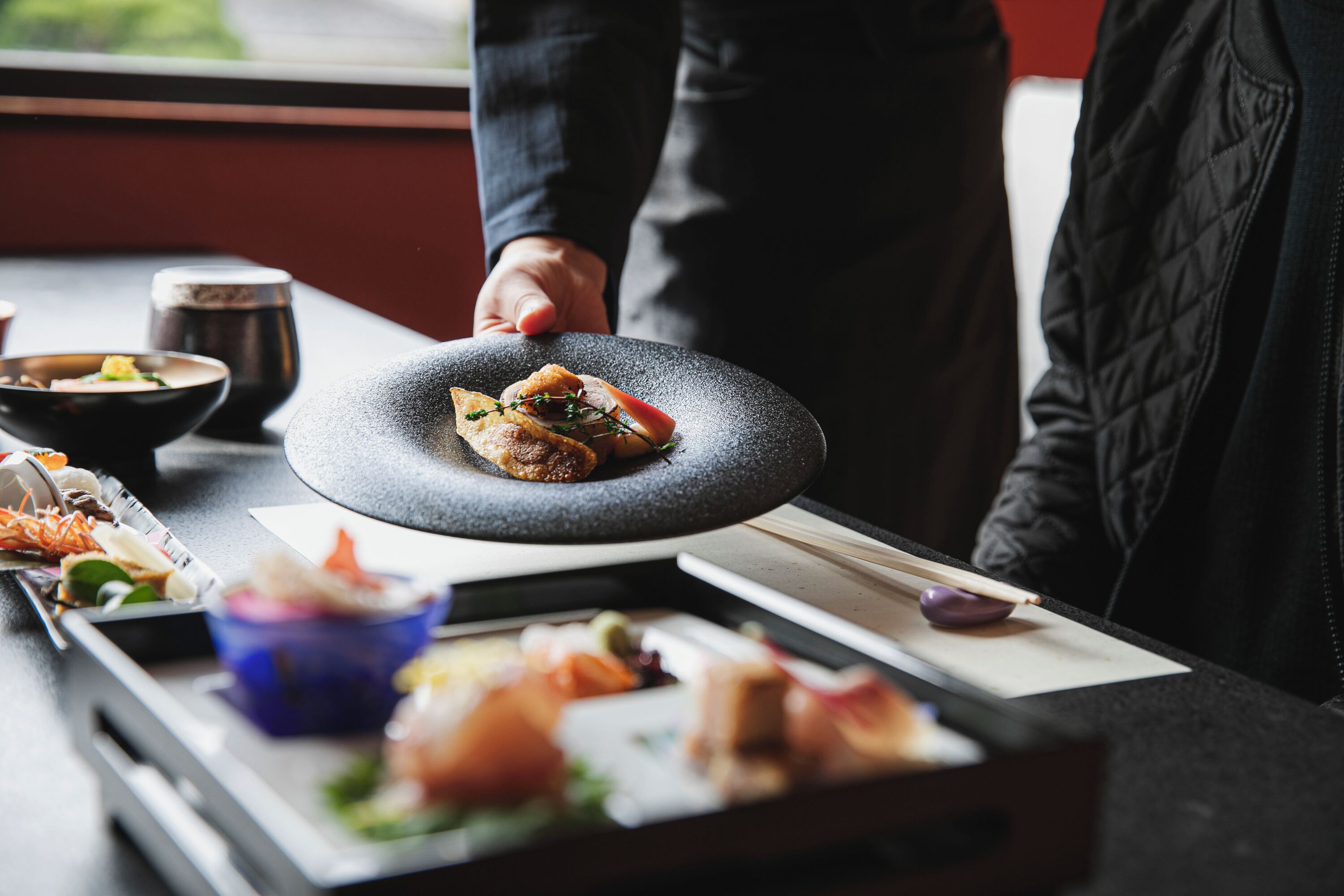 A dining table with various dishes, chopsticks, and a person serving food.