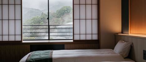 A traditional Japanese room with tatami flooring, a futon bed, and a shoji screen window overlooking a mountainous landscape.