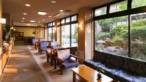 A hotel lobby with a long reception desk, seating area with sofas and chairs, large windows with a view of a garden, and a carpeted floor. - Ureshino Motoyu (Ureshino)