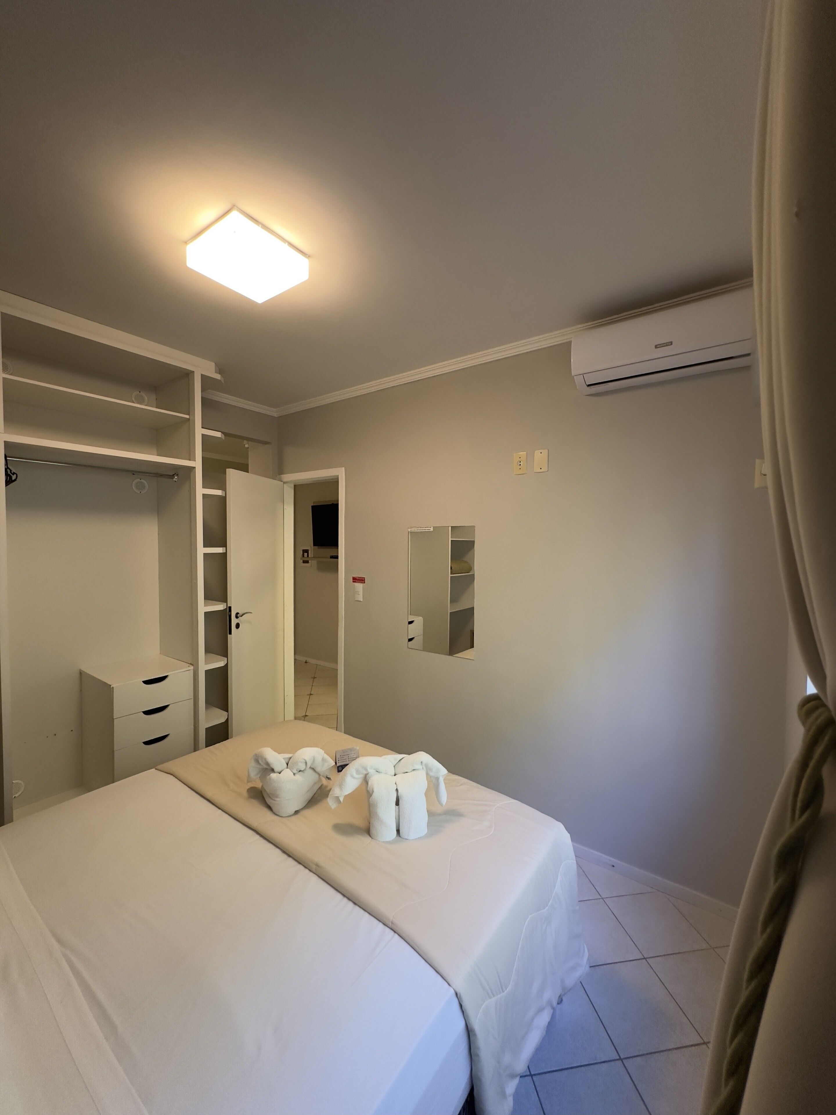 A hotel room with a bed, a wardrobe, a mirror, and an air conditioning unit.