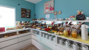 En buffet med forskellige retter og drikkevarer, et skilt med teksten "Bem Dia", og et vindue med udsigt til spisende mennesker.