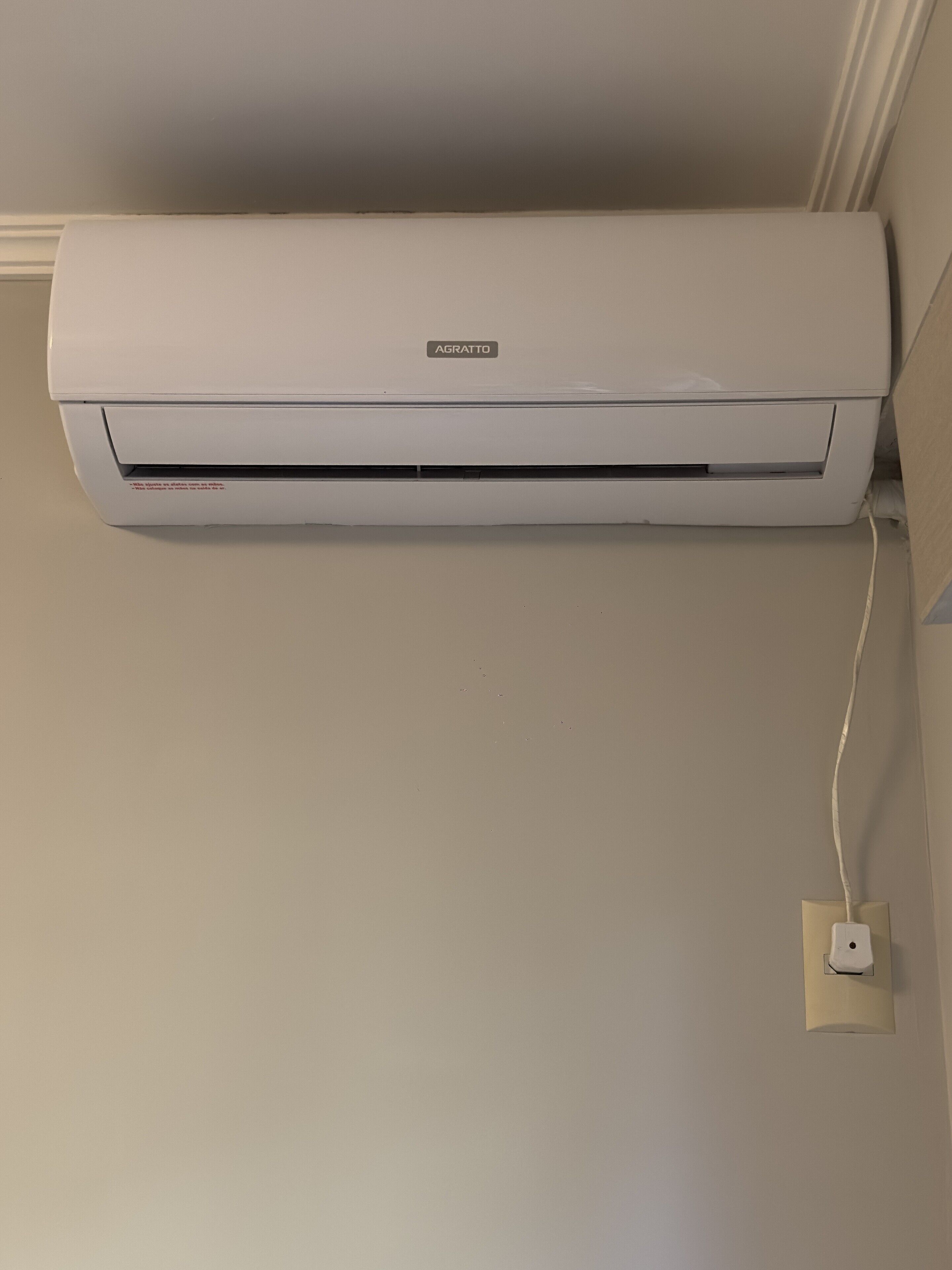 A white air conditioning unit mounted on a wall with a visible power outlet below it.