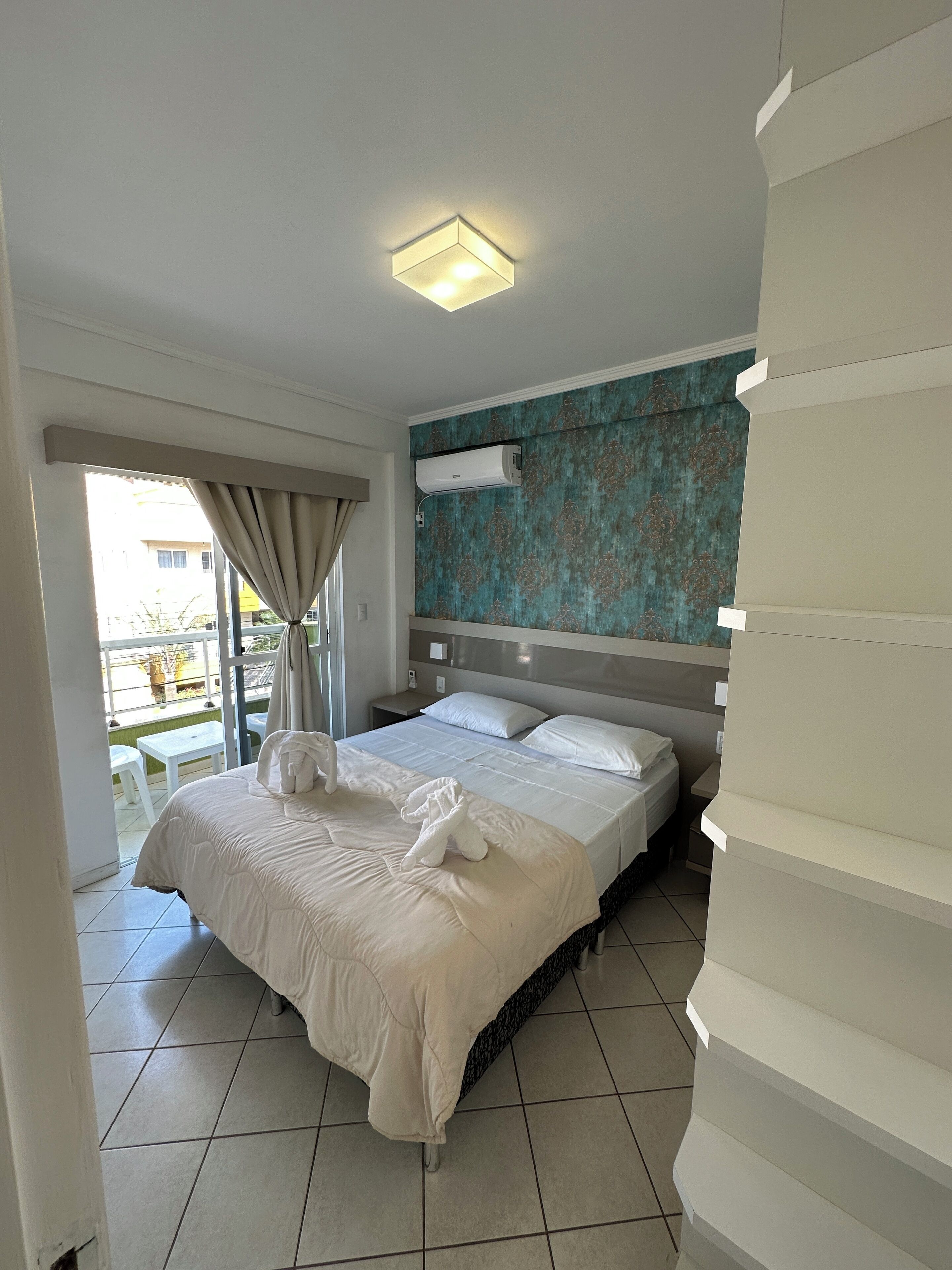 Ein Hotelzimmer mit einem Bett, einem Nachttisch, einer Wand-Klimaanlage und Blick auf den Balkon.