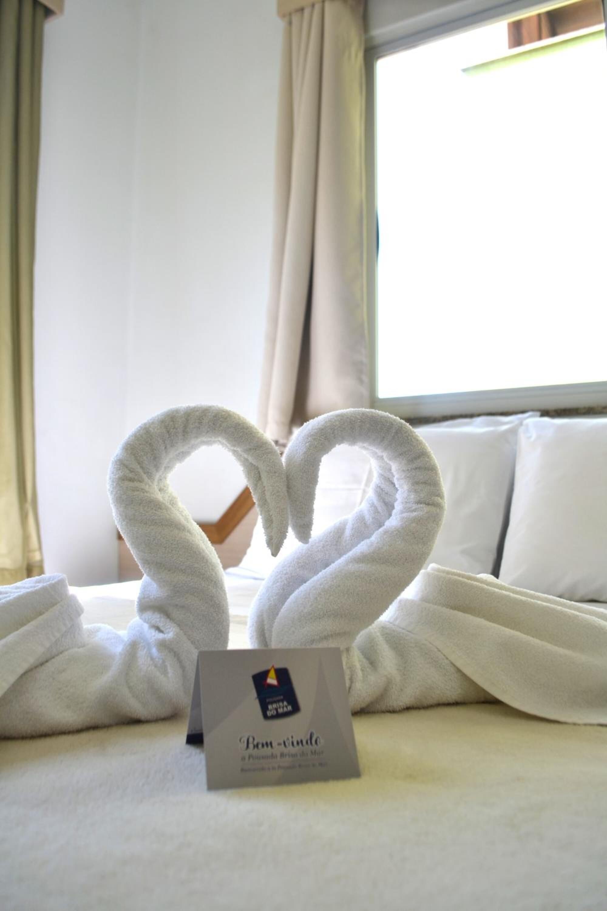 Una cama con dos toallas dispuestas en forma de corazón y una tarjeta sobre la cama.