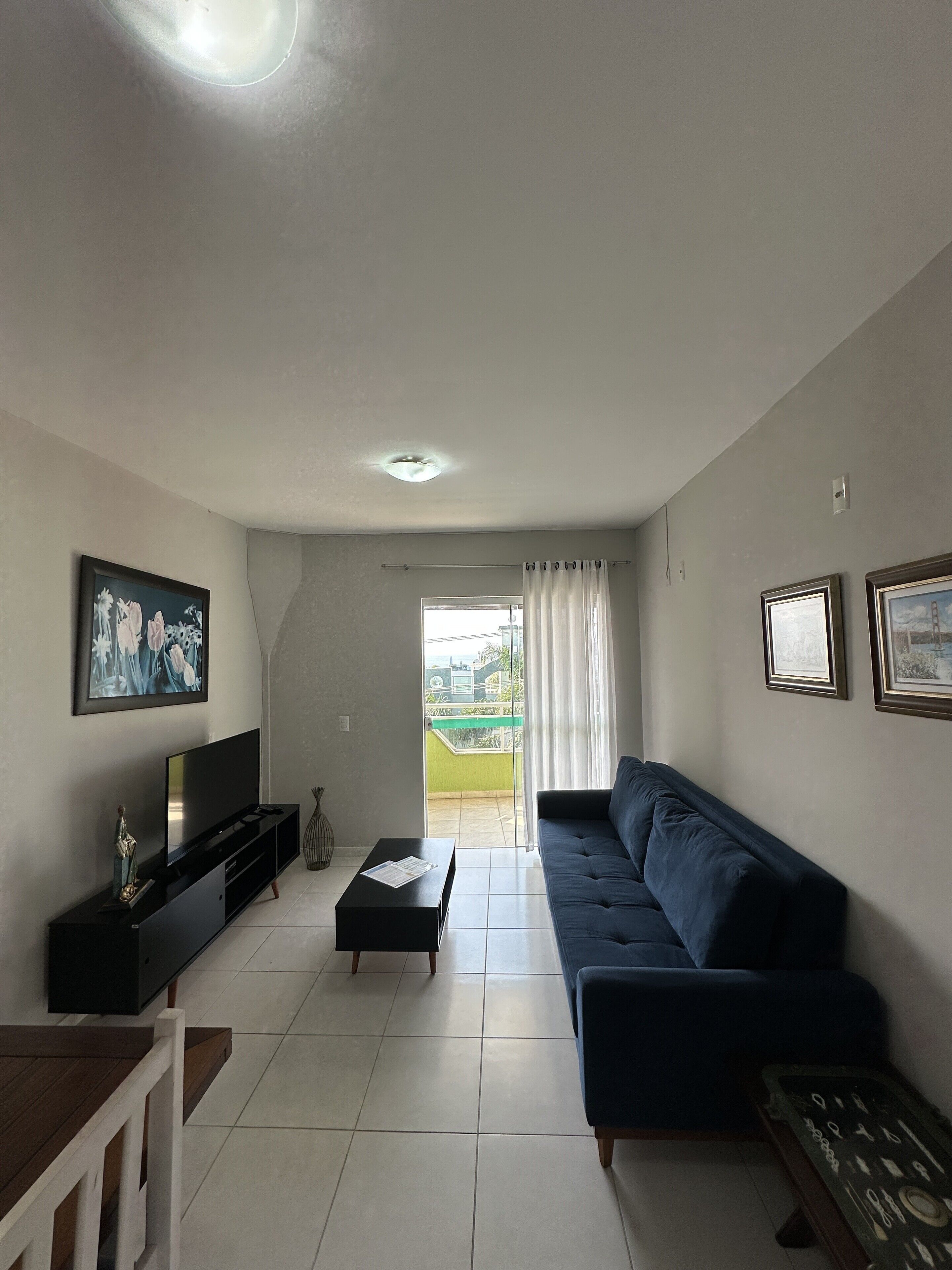 Un soggiorno con una TV a schermo piatto, un divano blu scuro, un tavolino da caffè e vista su un paesaggio verde attraverso una porta scorrevole in vetro.