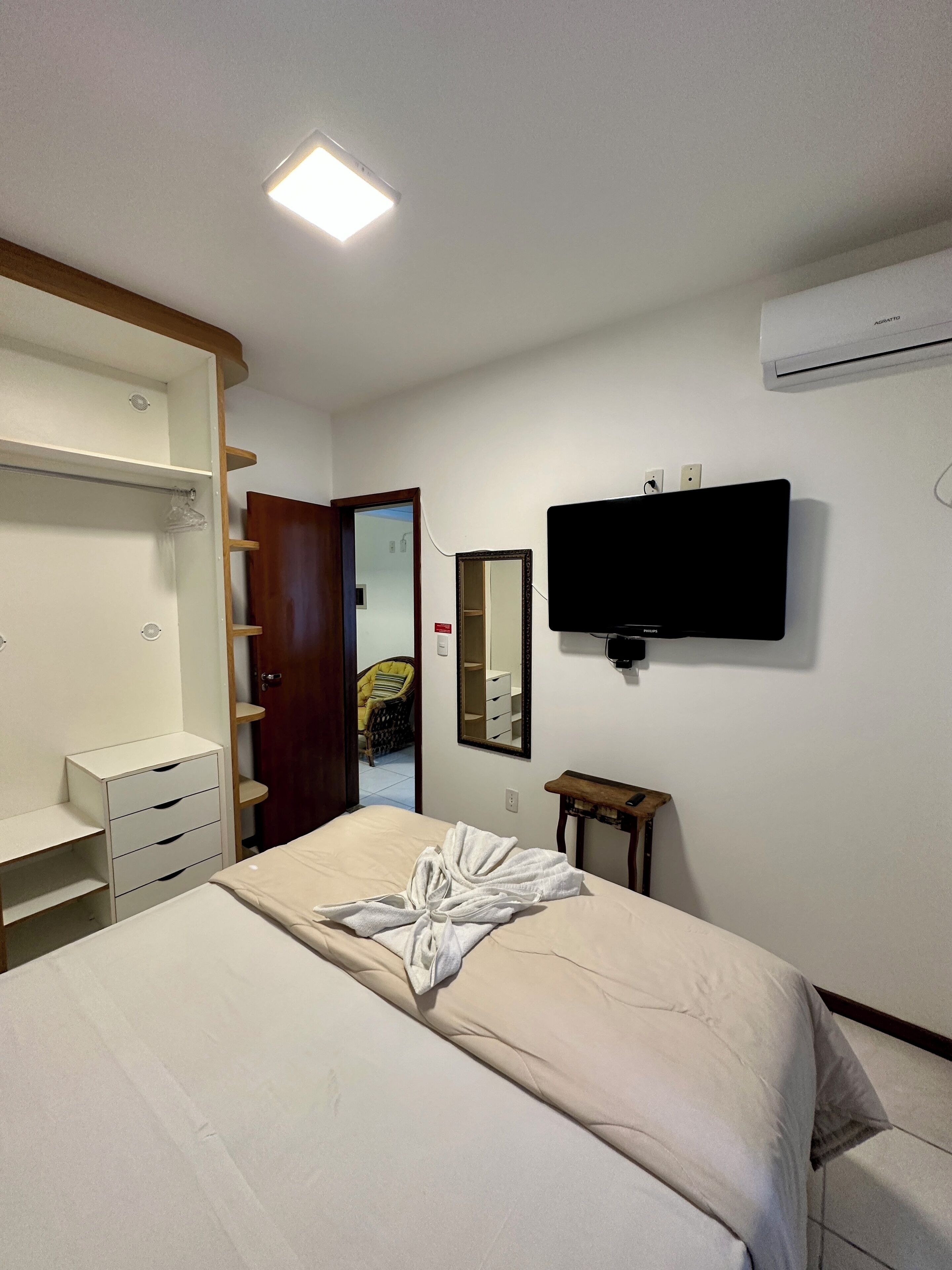 Habitación de hotel con cama, armario, espejo, televisor y aire acondicionado.