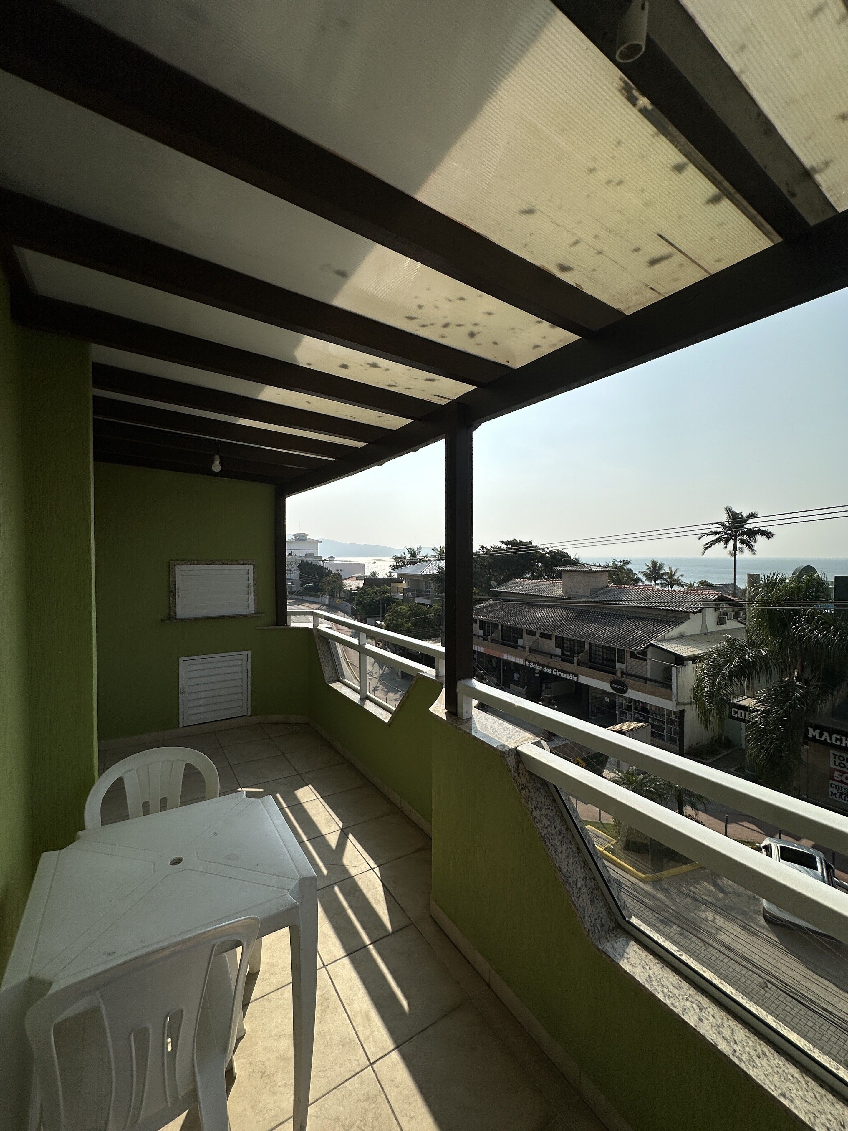 A balcony with a view of a cityscape, a white table, and a chair.