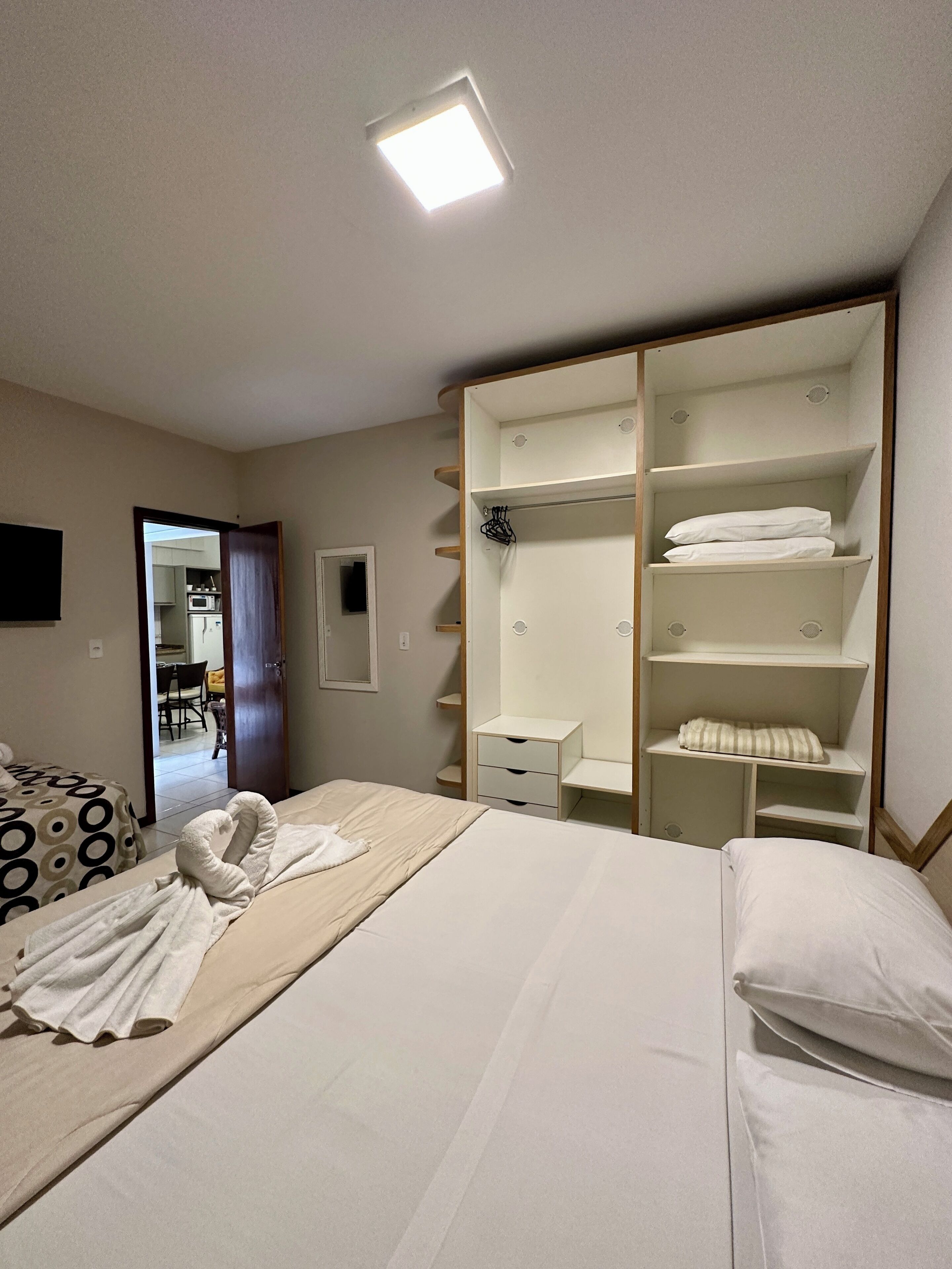Quarto de hotel com cama, guarda-roupa, escrivaninha e banheiro visível através de uma porta aberta.