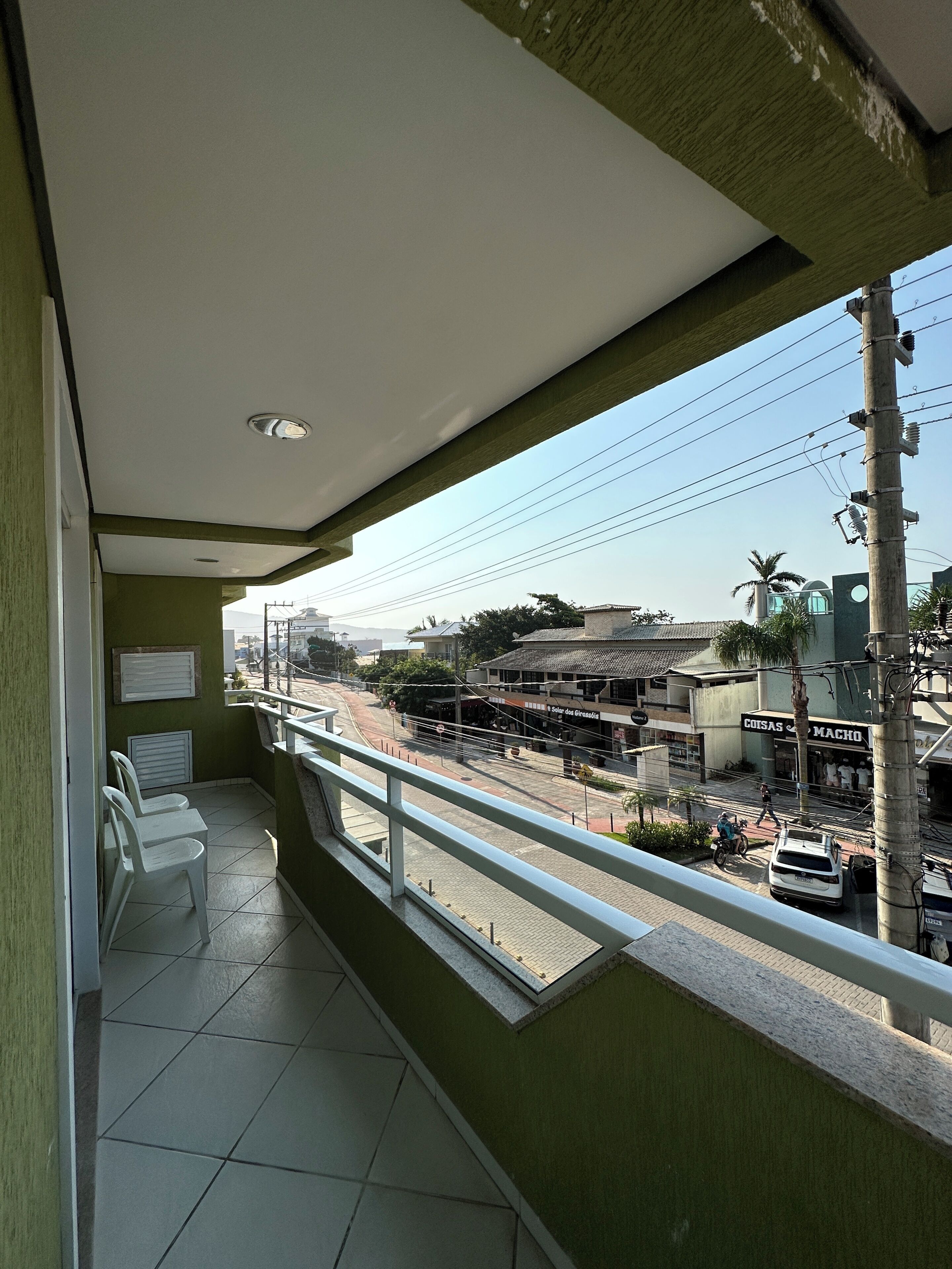 A balcony with a view of a street, a building with a sign, and a parked motorcycle.