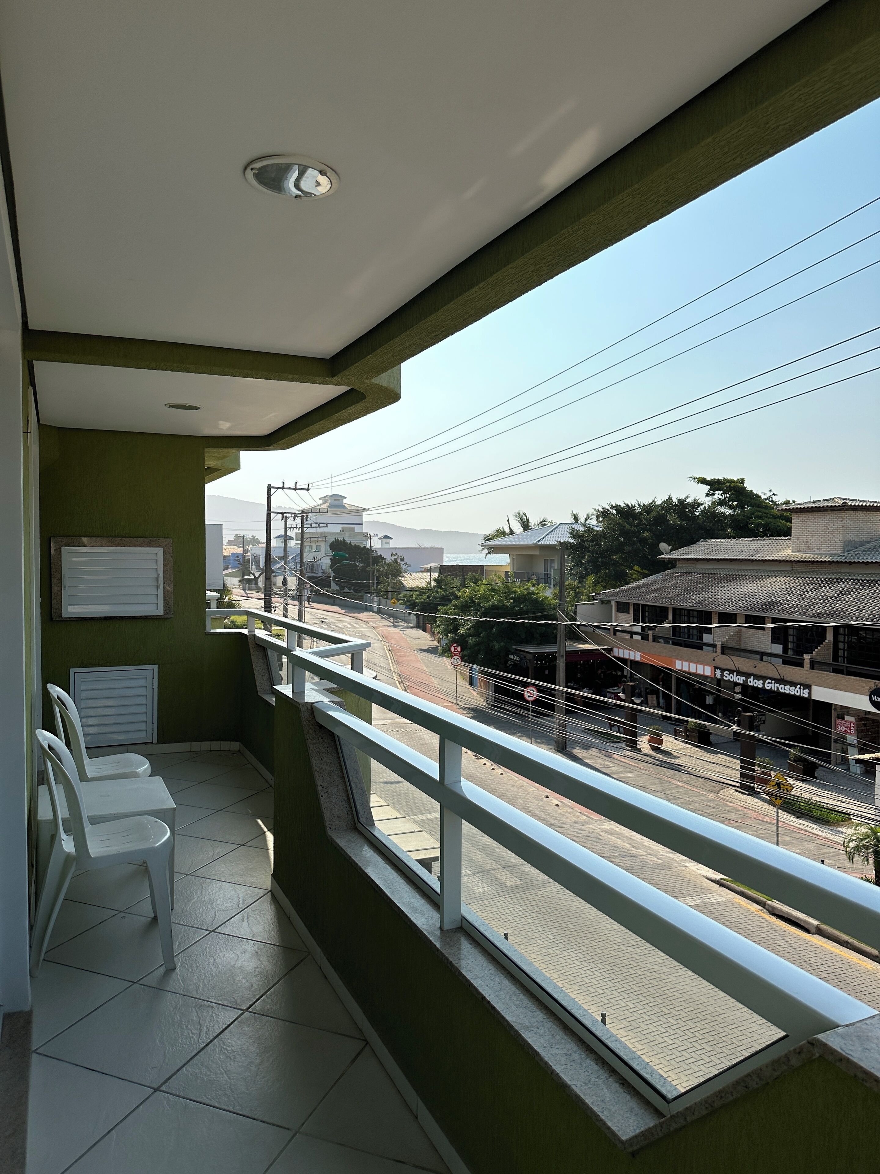 A balcony with a view of a street, a chair, and a sign for 'Solar dos Girassóis'.