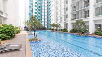 A modern indoor swimming pool with tiled flooring, surrounded by lush greenery and a white building with balconies.