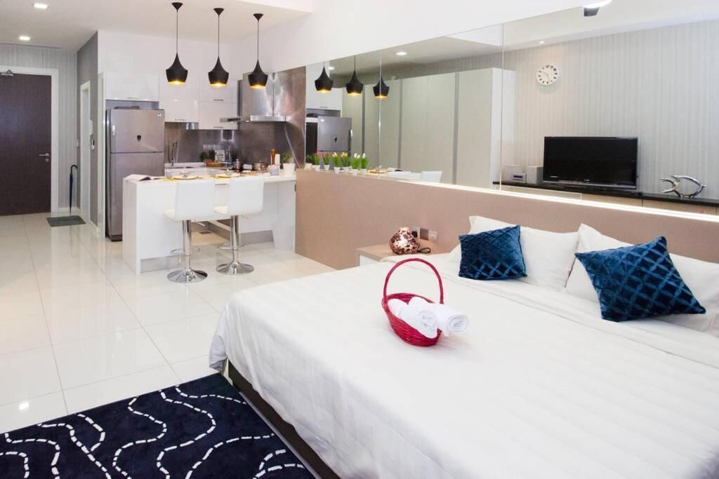 A modern hotel room with a large bed, a dining area, and a kitchen.