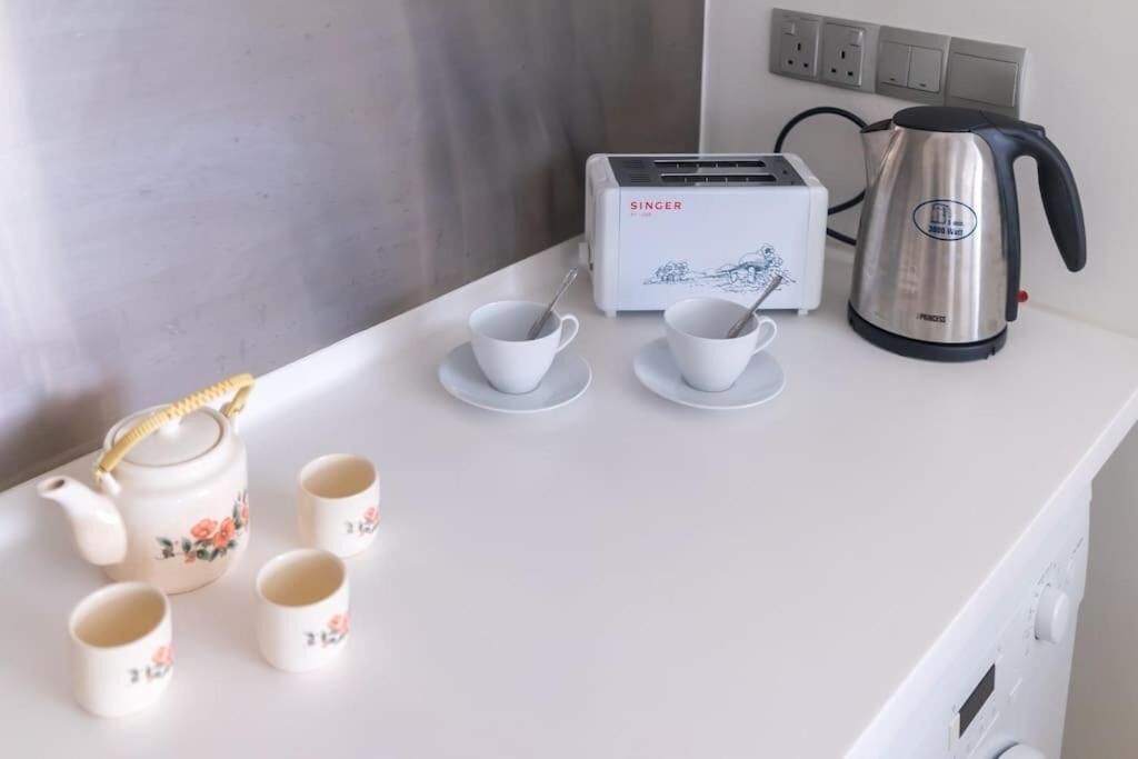 A kitchen counter with a toaster, a kettle, and teapots with cups.