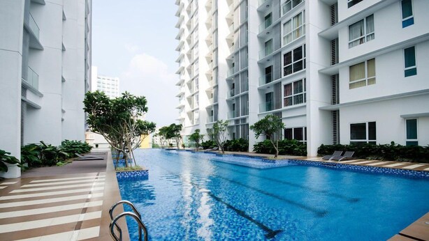 A modern building with a swimming pool, surrounded by greenery and a clear sky.