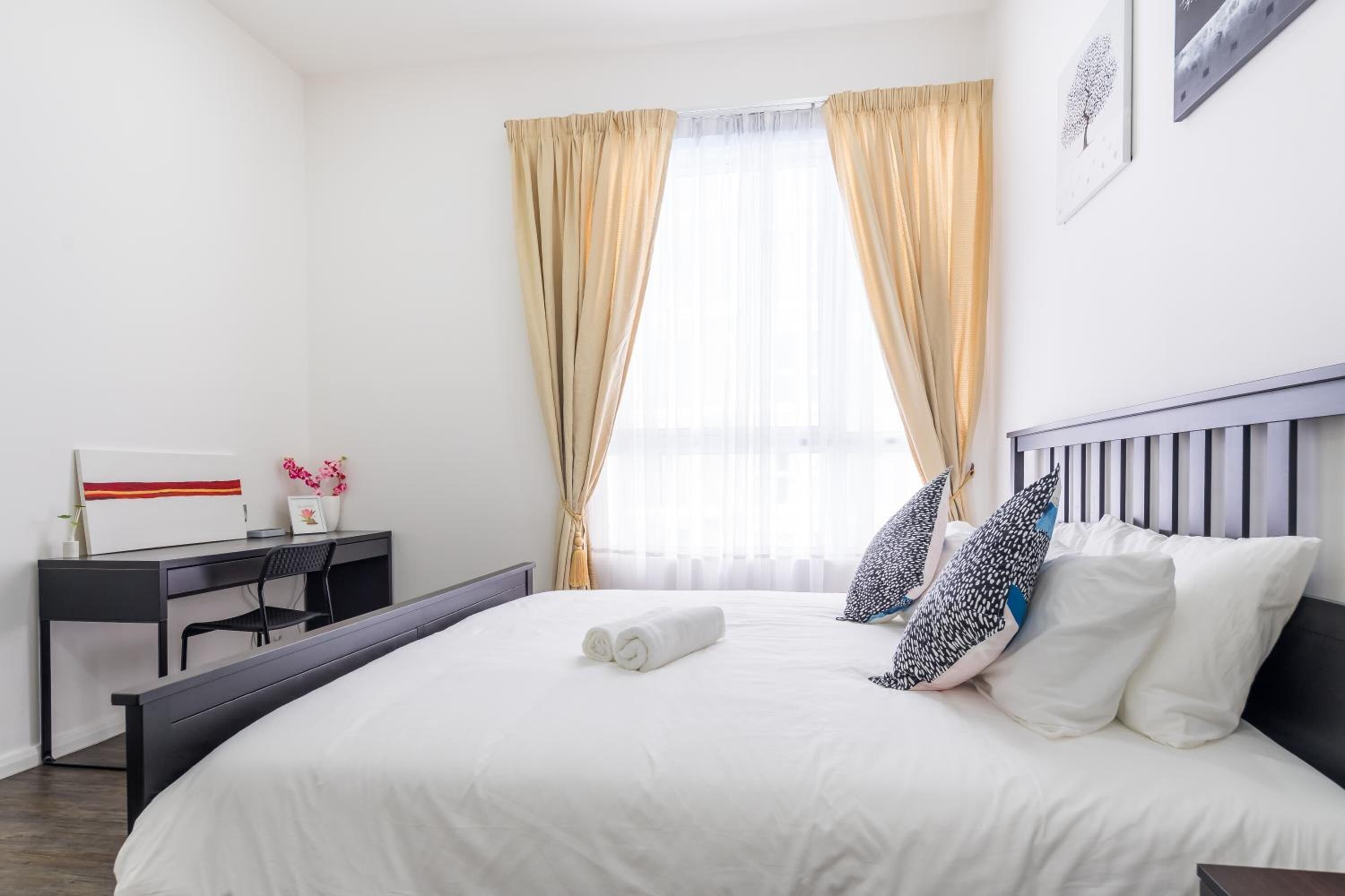 Une chambre d’hôtel bien rangée, avec un lit, un bureau et une fenêtre avec des rideaux.