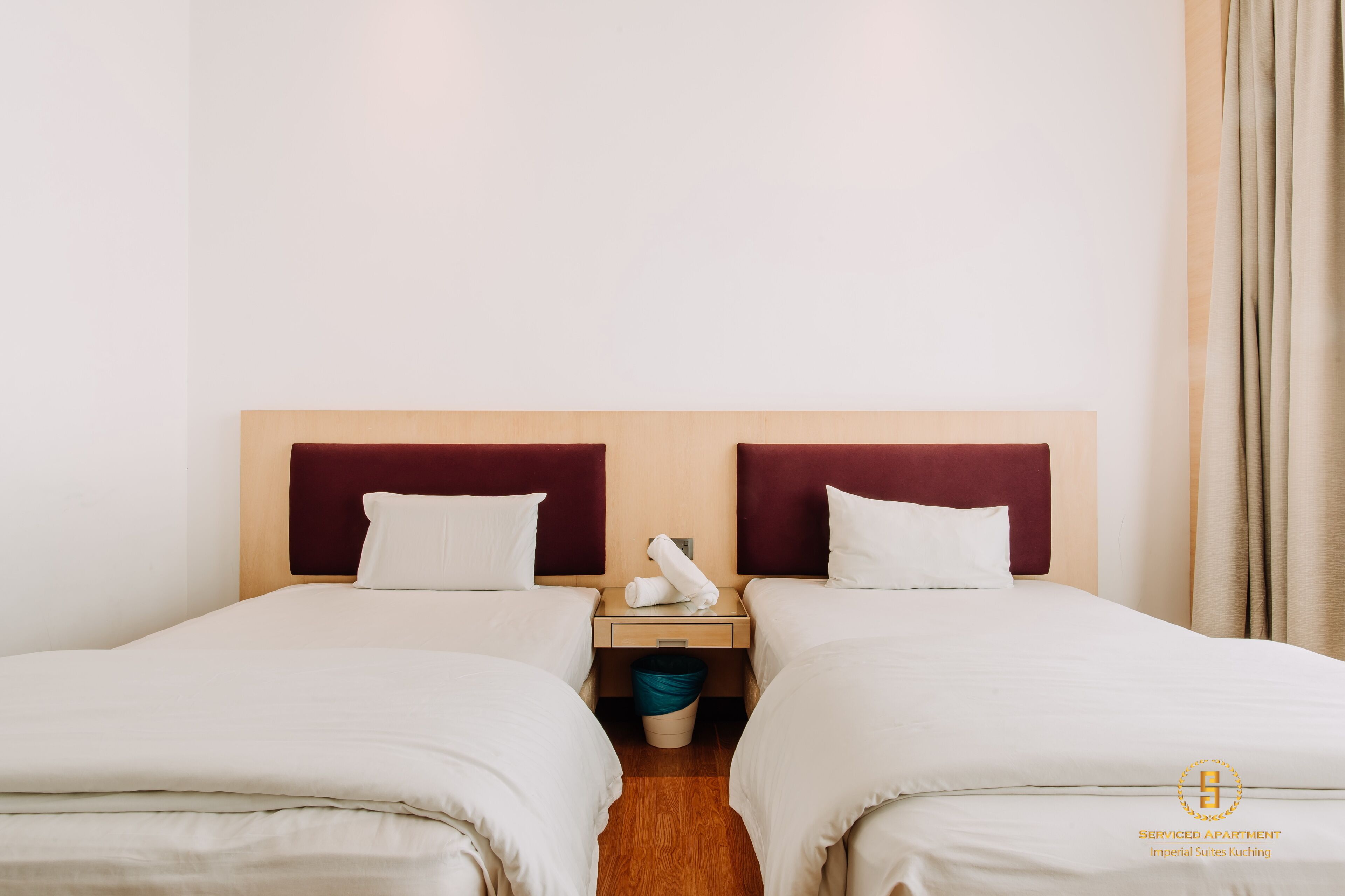 A double room with two beds, a nightstand, a trash bin, and a curtain.