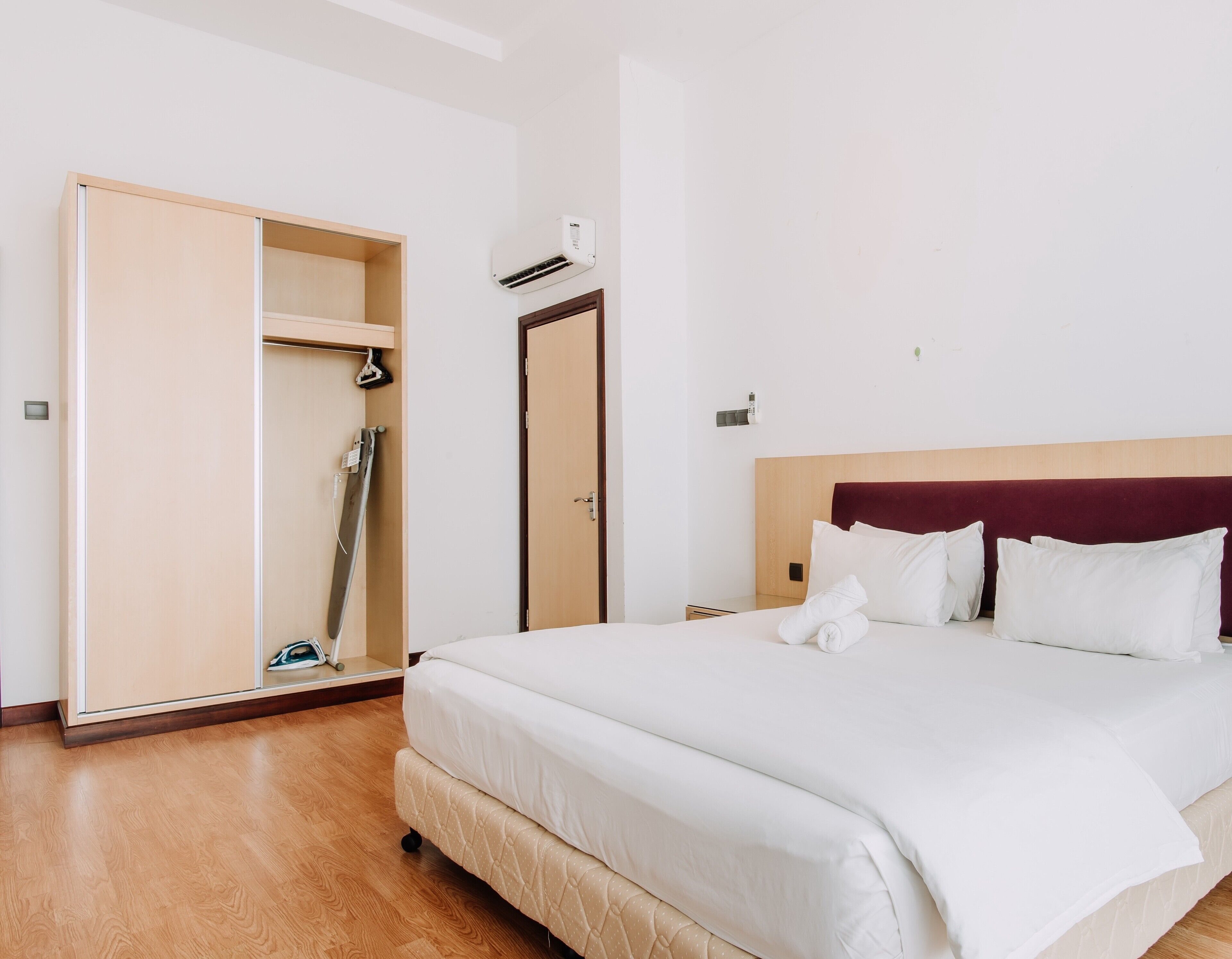 A hotel room with a bed, a wardrobe, a door, and an air conditioning unit.