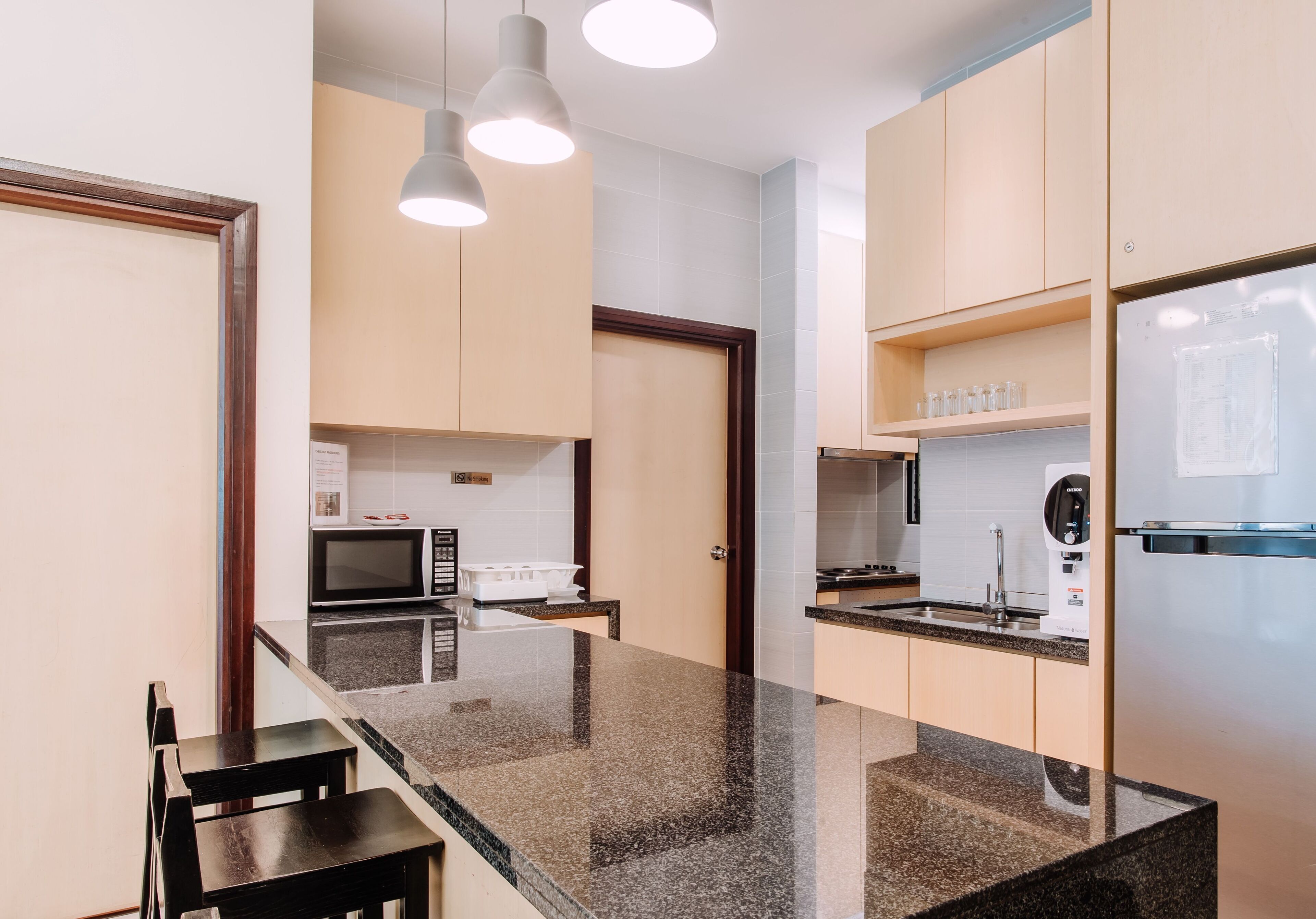 Una cocina moderna con encimeras de granito, microondas integrado y refrigerador. Hay dos sillas de madera y una pequeña mesa de comedor.