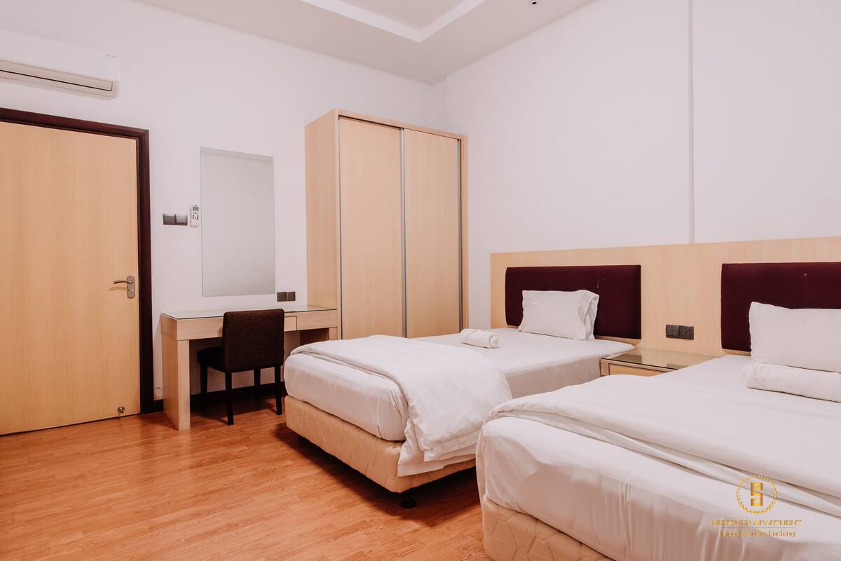 A hotel room with two beds, a desk, a chair, and a wardrobe.