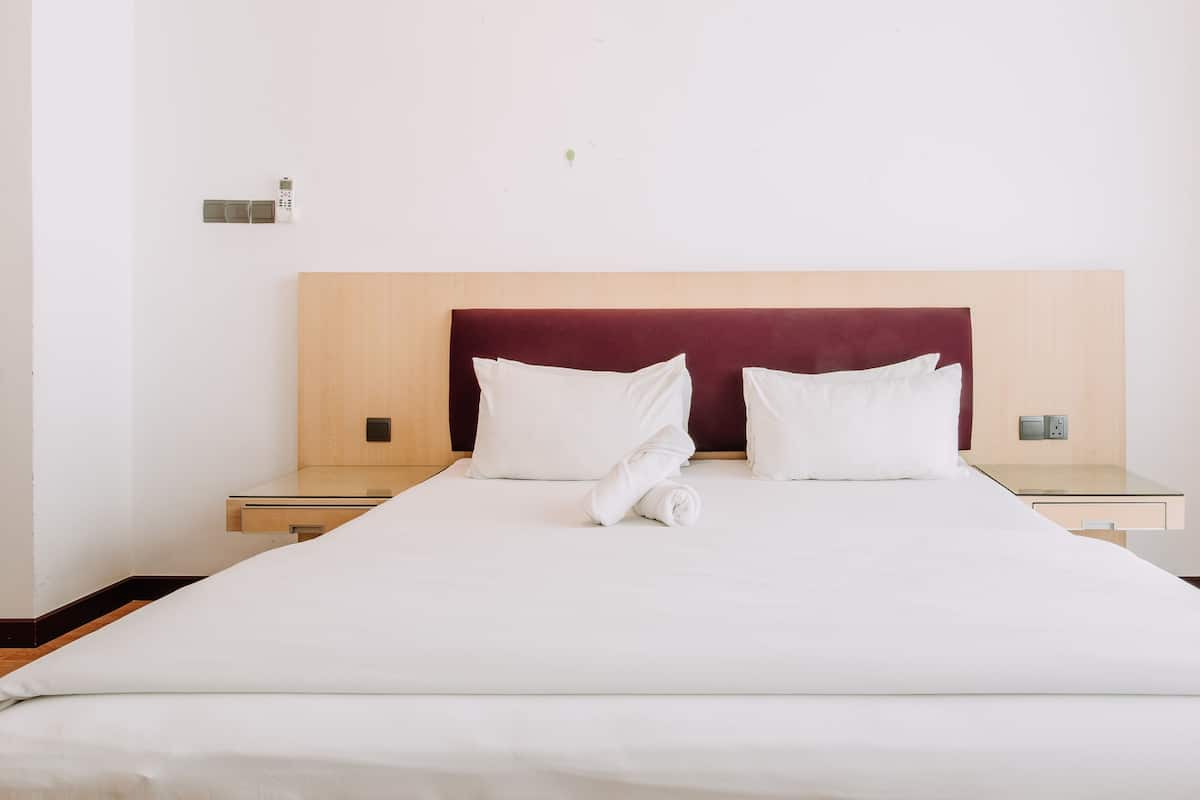 A neatly made bed with white linens and a wooden headboard. There are two bedside tables with a small lamp on each.