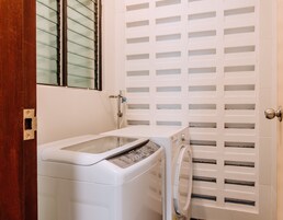 Un área de lavandería compacta con lavadora y secadora, una ventana con persianas y una puerta con diseño de listones.
