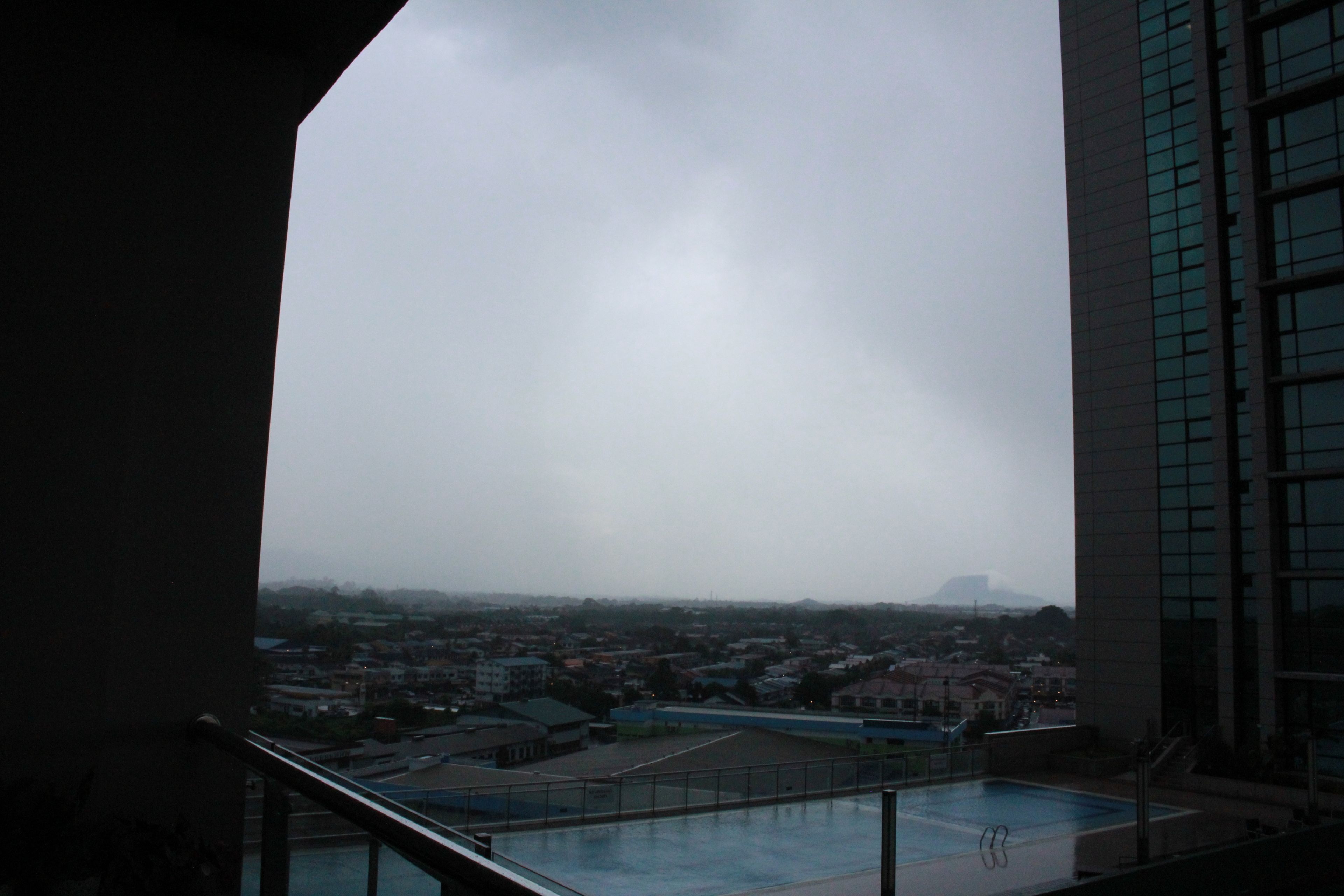 A rooftop pool with a view of a cityscape and a cloudy sky.