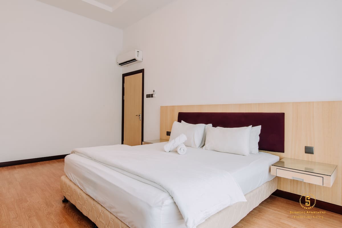 A neatly made bed with white linens, a wooden headboard, and a bedside table with a glass top.