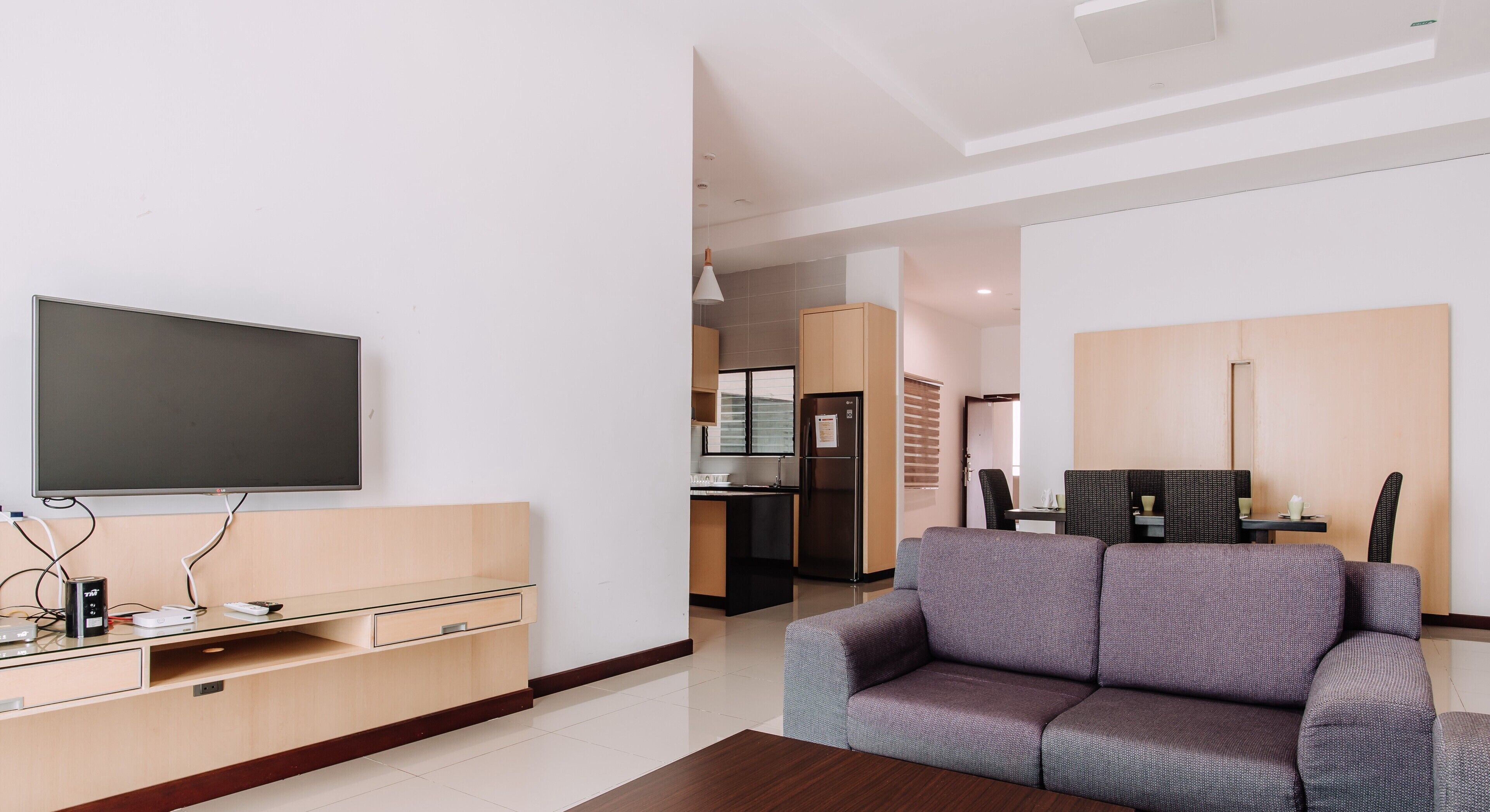 A modern living room with a flat-screen TV, a sofa, and a dining area with a table and chairs.
