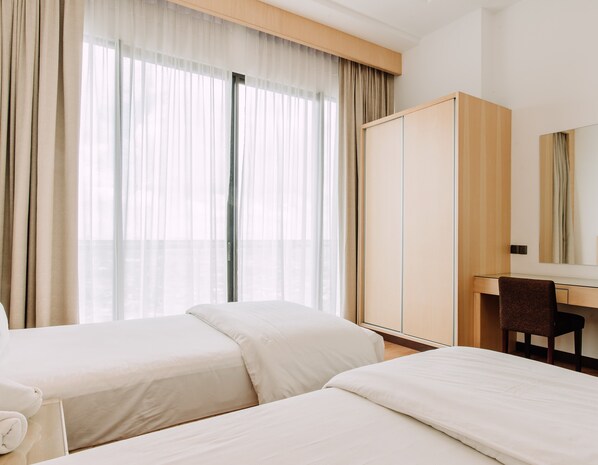 Habitación de hotel con dos camas, un escritorio, una silla, un armario y un ventanal con cortinas traslúcidas.