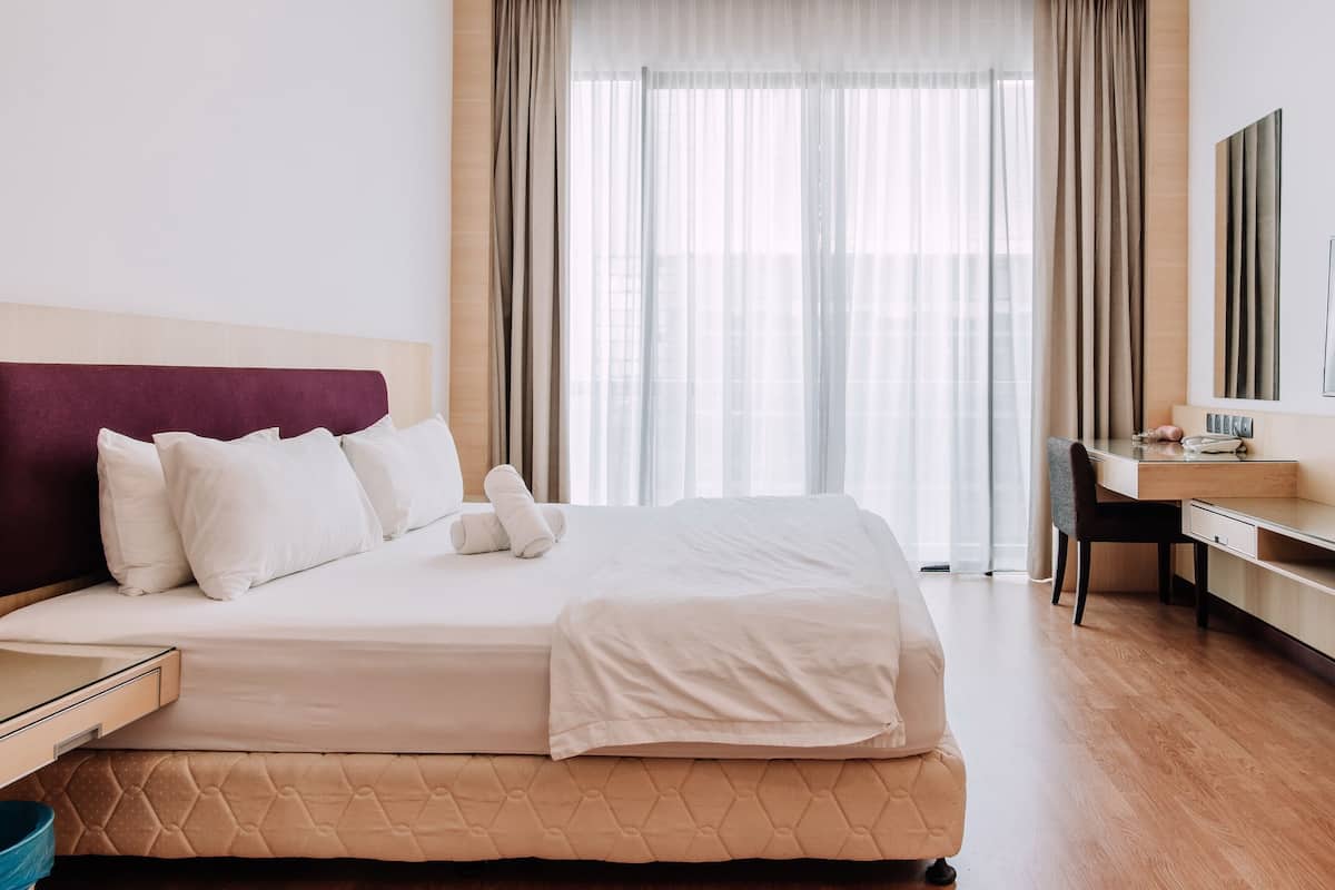 A hotel room with a bed, a desk, and a large window with curtains.