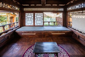 A traditional Japanese-style room with tatami flooring, a low wooden bed with storage drawers, a small table, and a view of the garden through shoji screens. - Soi Hanok Stay (Gyeongju)