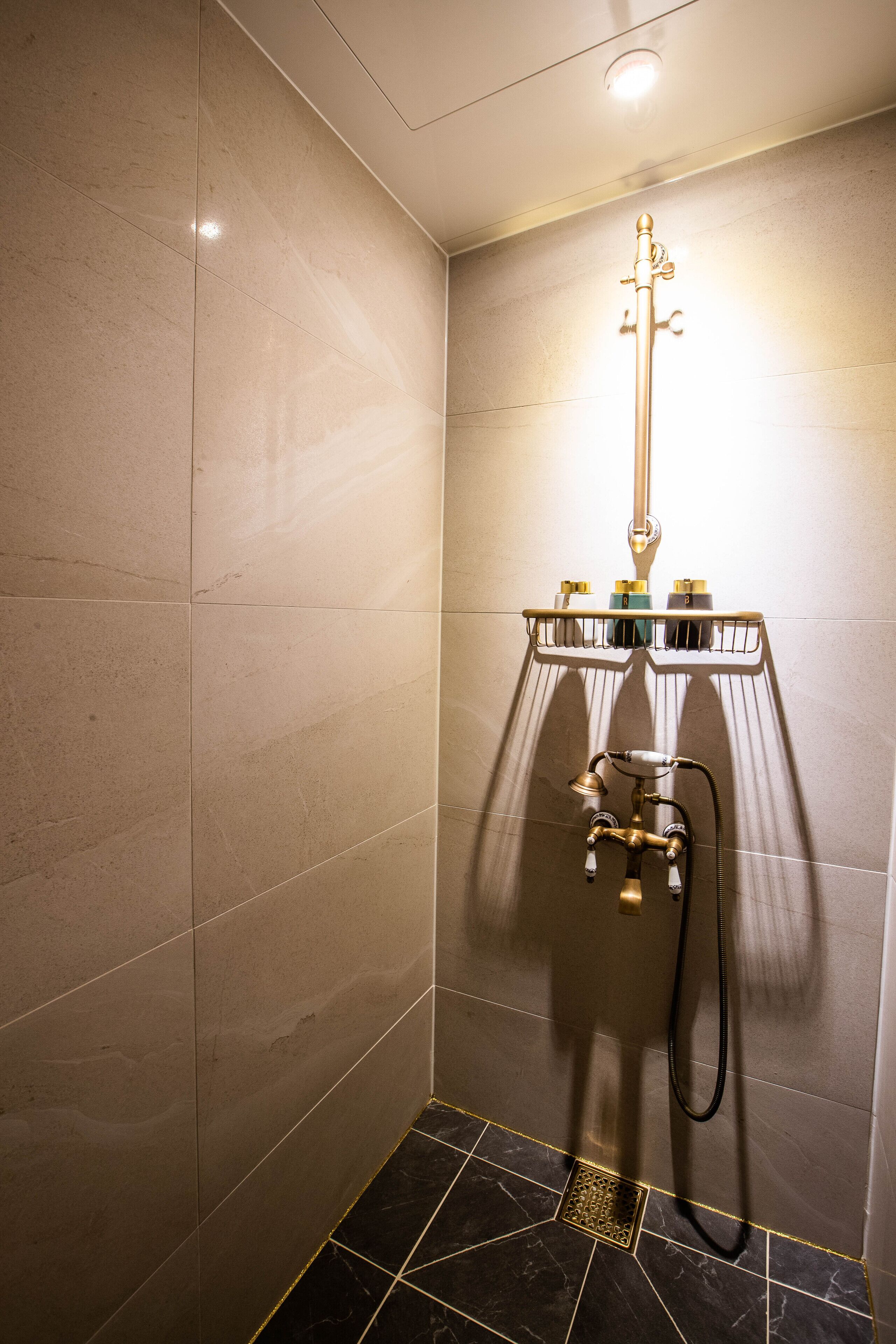 A modern shower with a handheld showerhead, a control panel, and a drain.