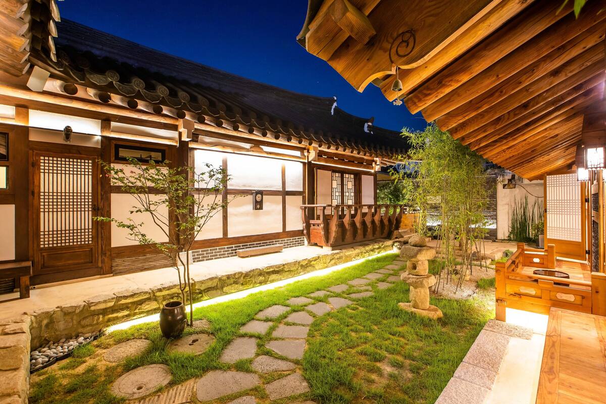 A traditional Japanese building with a wooden exterior, stone pathway, and a small garden area with a tree and a stone lantern.