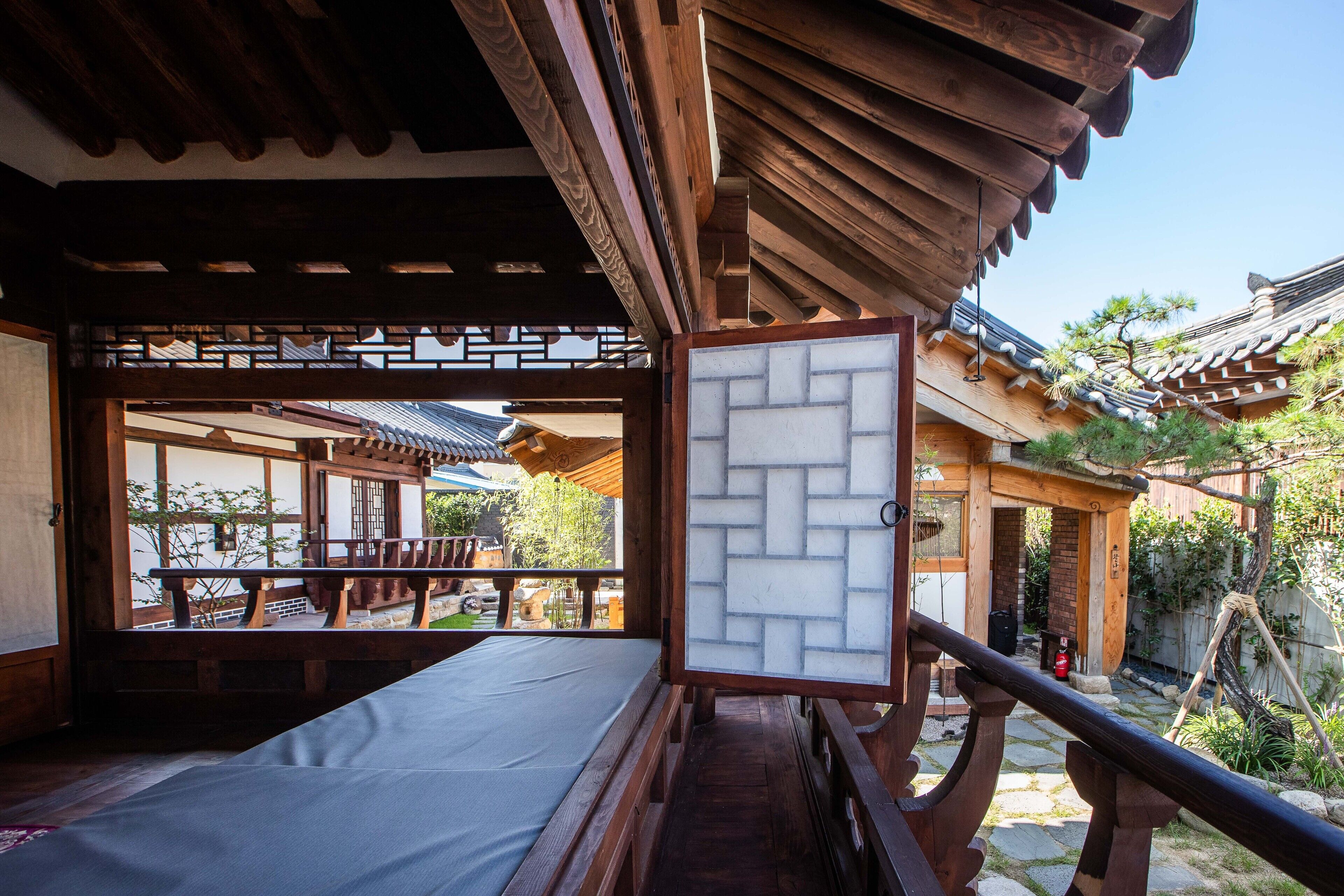 Una tradizionale stanza in stile giapponese con pavimento in tatami, una porta scorrevole e vista sul giardino e sugli edifici vicini.