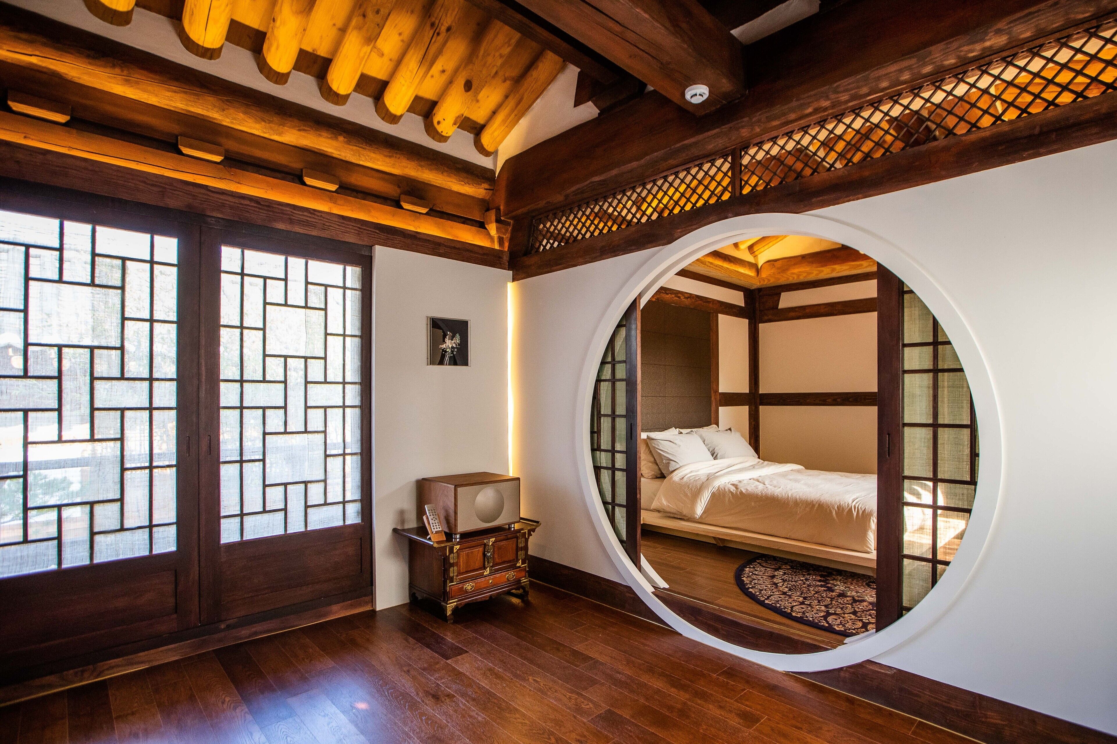 A traditional Japanese-style room with tatami flooring, a round window, and a bed with a futon.