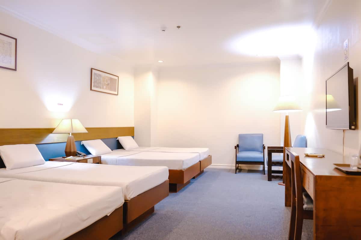 A hotel room with two single beds, a desk with a chair, a small table, and a TV.