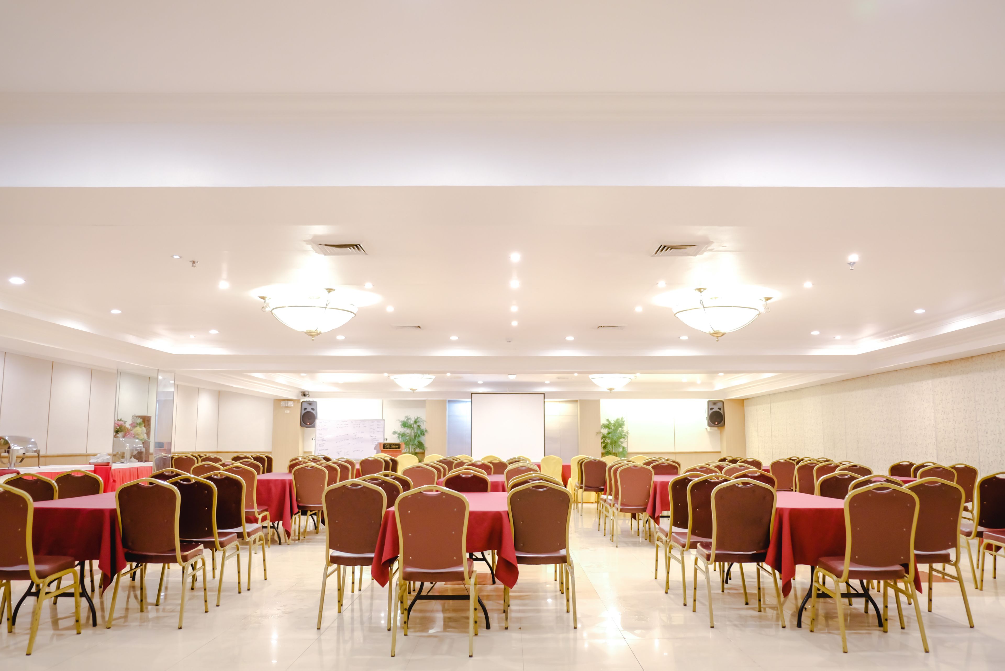A conference room with rows of tables and chairs, equipped with ceiling lights and speakers.