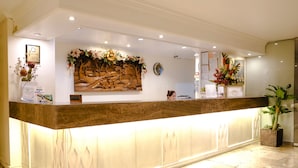 A reception desk with a marble top, a large floral arrangement above it, and a framed artwork on the wall. - De Luxe Hotel (Cagayan de Oro)