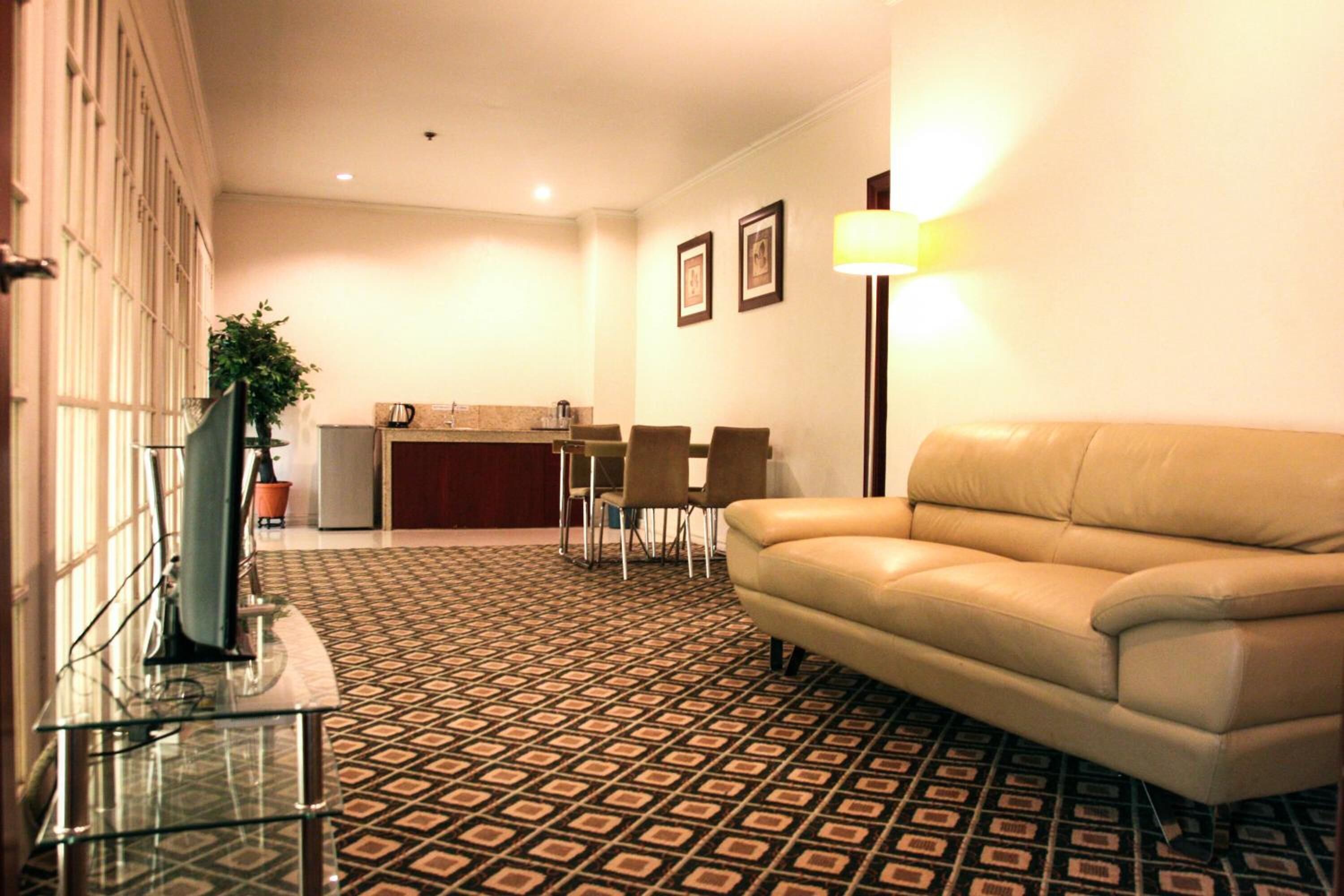 A hotel lobby with a patterned floor, a leather sofa, a glass coffee table, a reception desk, and framed pictures on the wall.