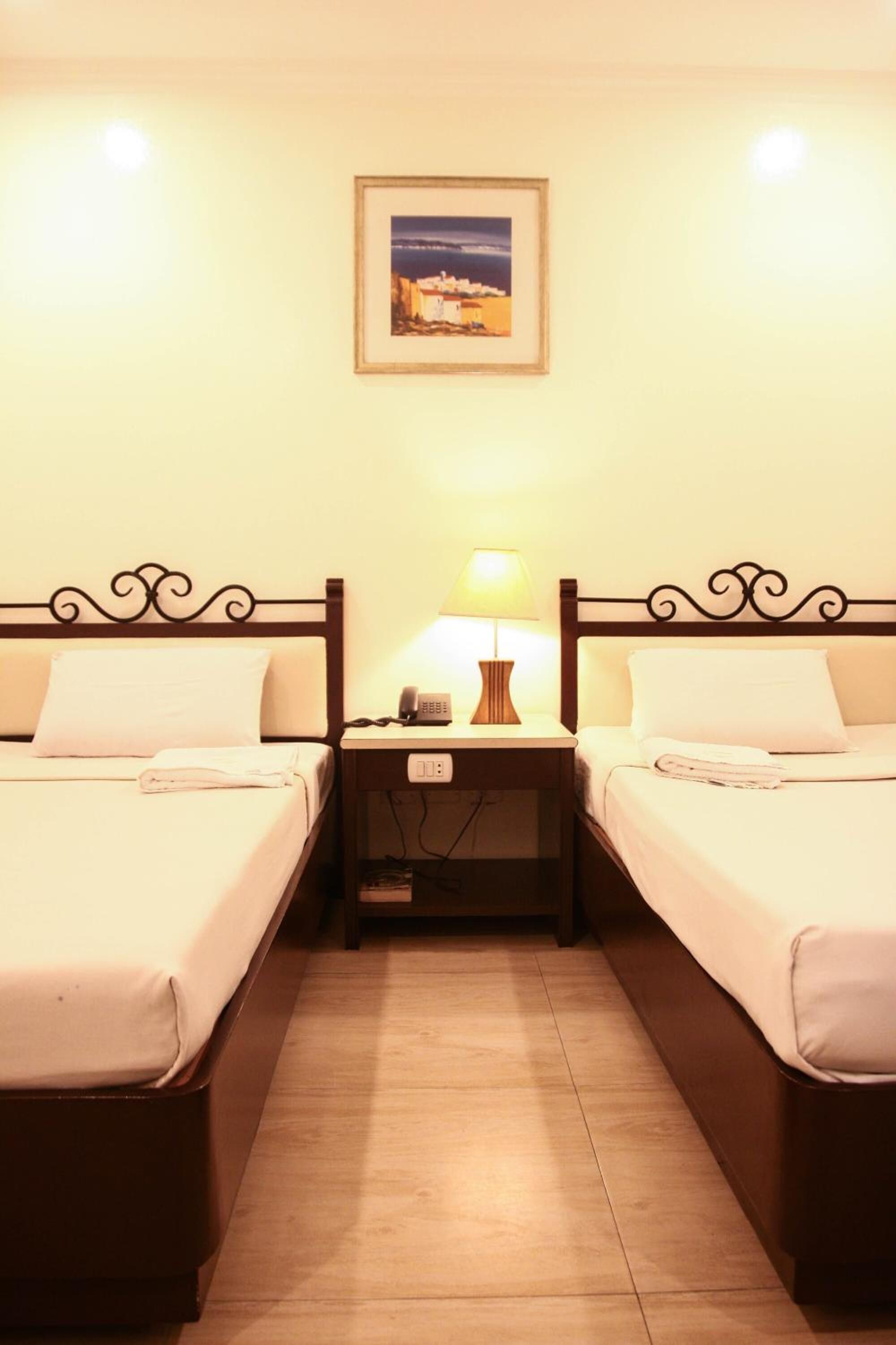 Una habitación de hotel con dos camas, una mesita de noche con una lámpara, un teléfono y un cuadro en la pared.