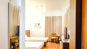 A hotel room with two beds, a desk, a chair, a TV, and a window with curtains. - De Luxe Hotel (Cagayan de Oro)
